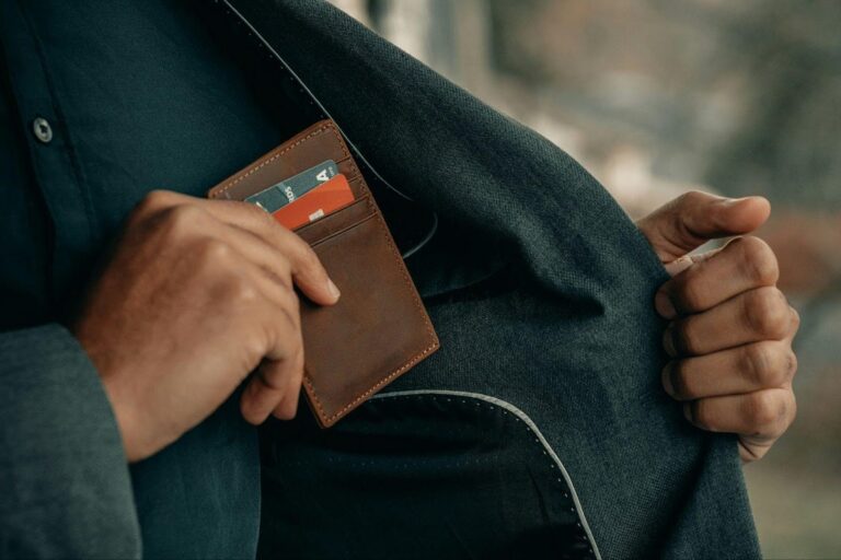 Close-up of a man placing a leather wallet with credit cards into the inside pocket of a suit jacket – representing secure digital finance, modern banking, and professional money management